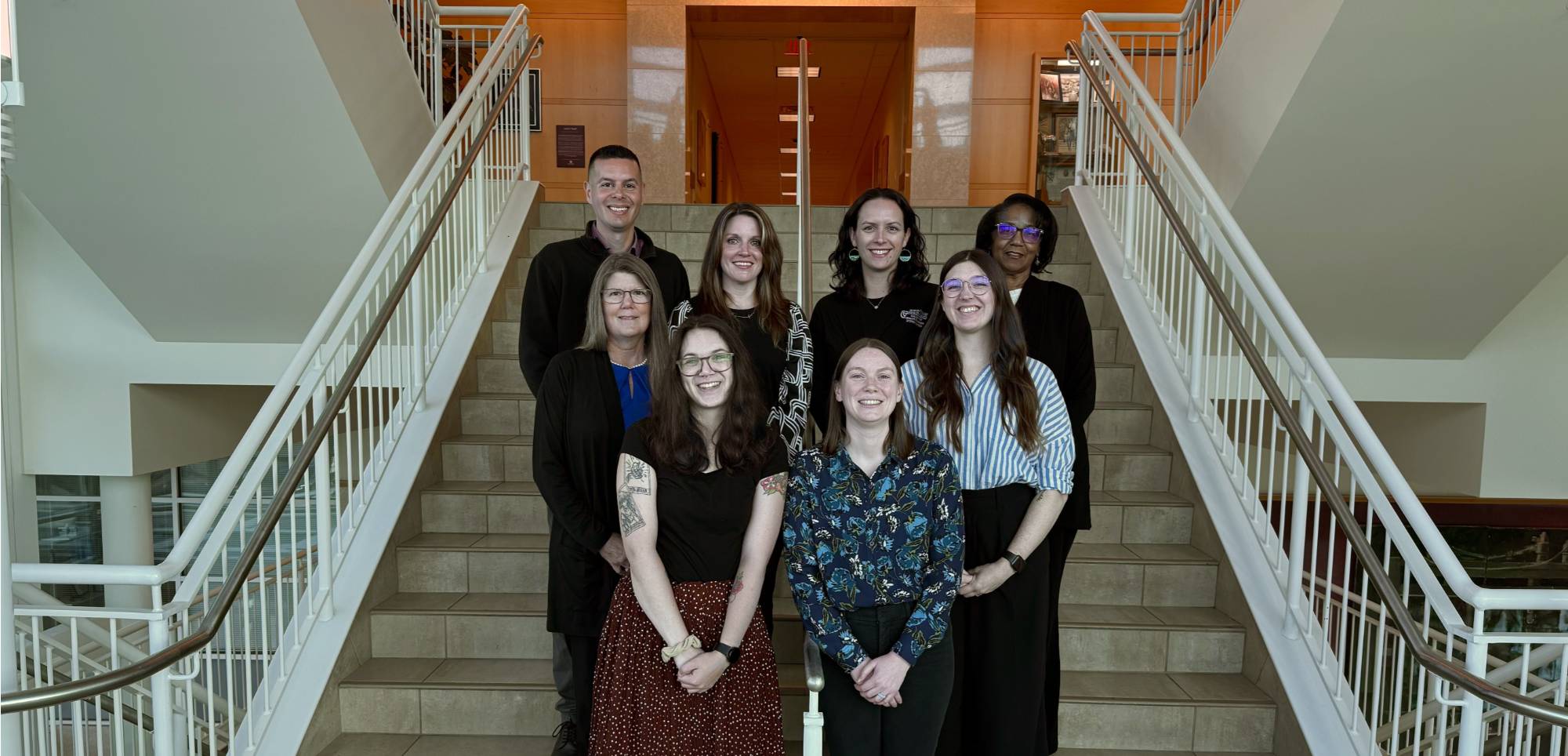 Group photo of CHP Student Services Office standing on a staircase in the Center for Health Sciences building